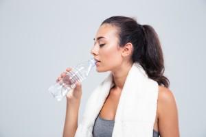 Portrait of a fitness woman with towel drinking water isolated on a white background